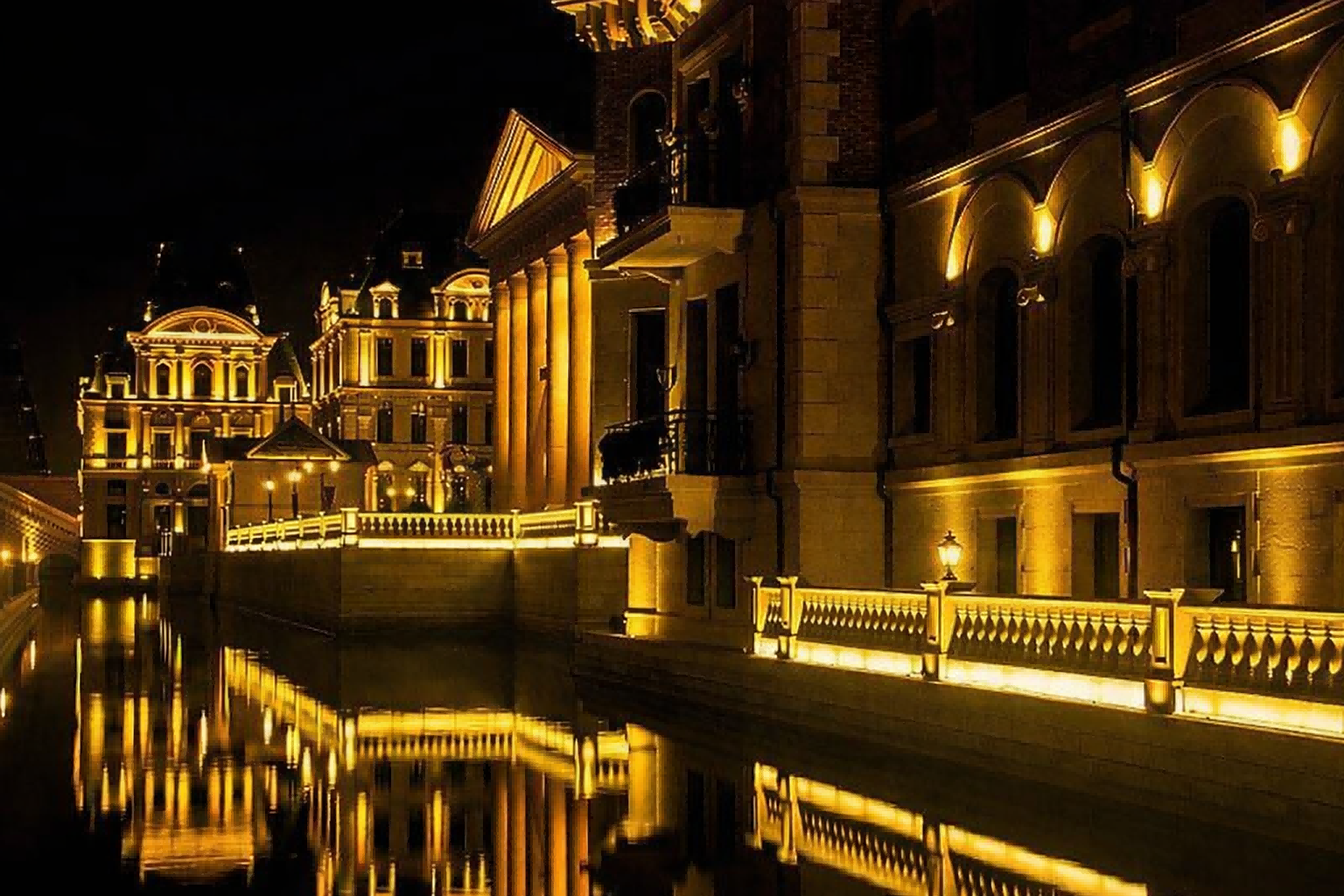 Warm golden LED flood lights illuminating classical-style buildings and railings reflecting in a canal, creating an inviting public atmosphere.