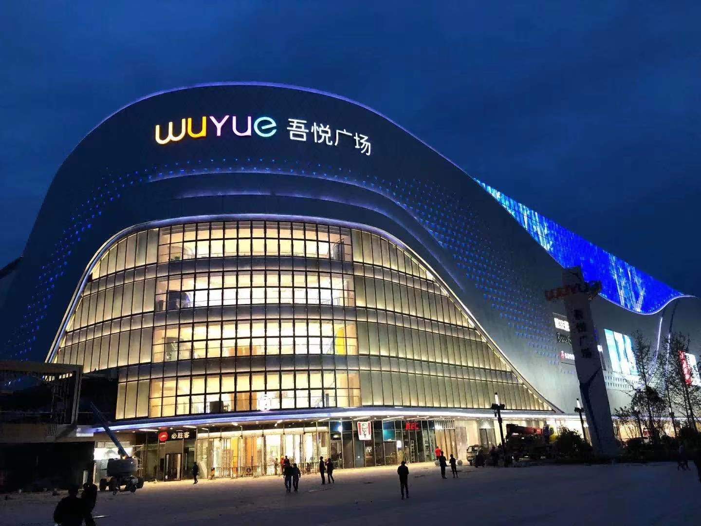 WUYUE curved mall façade illuminated at night with blue media lighting and warm interior glow